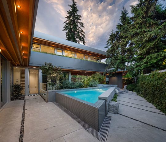 Outdoor space of a custom-built North Vancouver home. Shows an outdoor pool, lighting, and a custom-designed exterior.