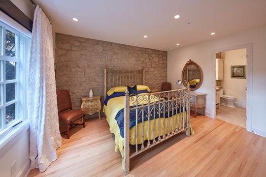 Custom built guest bedroom with stone wall, wooden flooring, and separate bathroom.