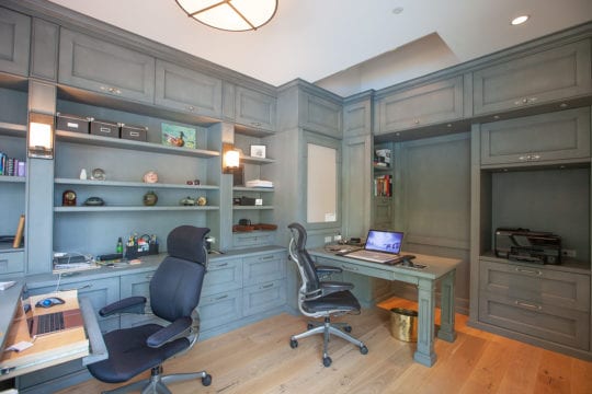 Custom-built office space with wooden flooring, two desks, and blue-grey shelves.
